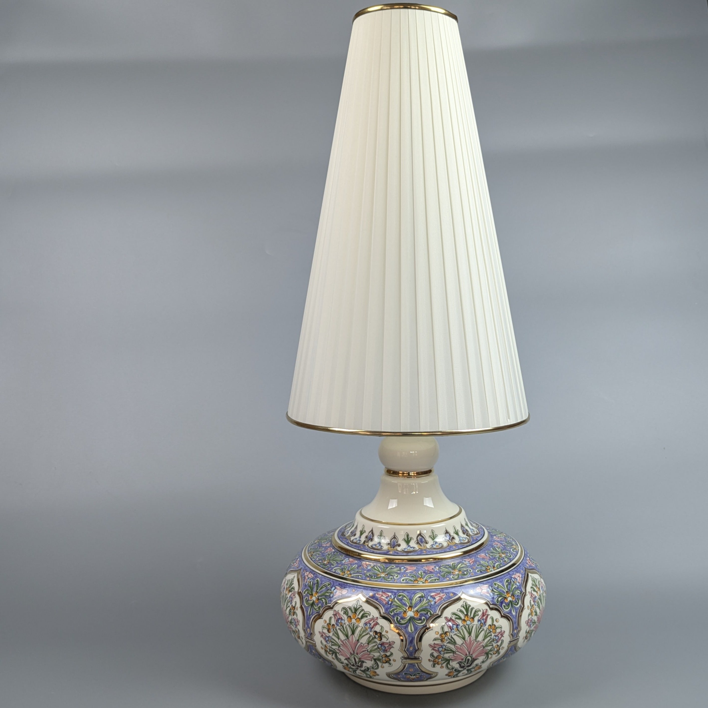 Decorative table lamp with a floral base and pleated white shade on a gray background