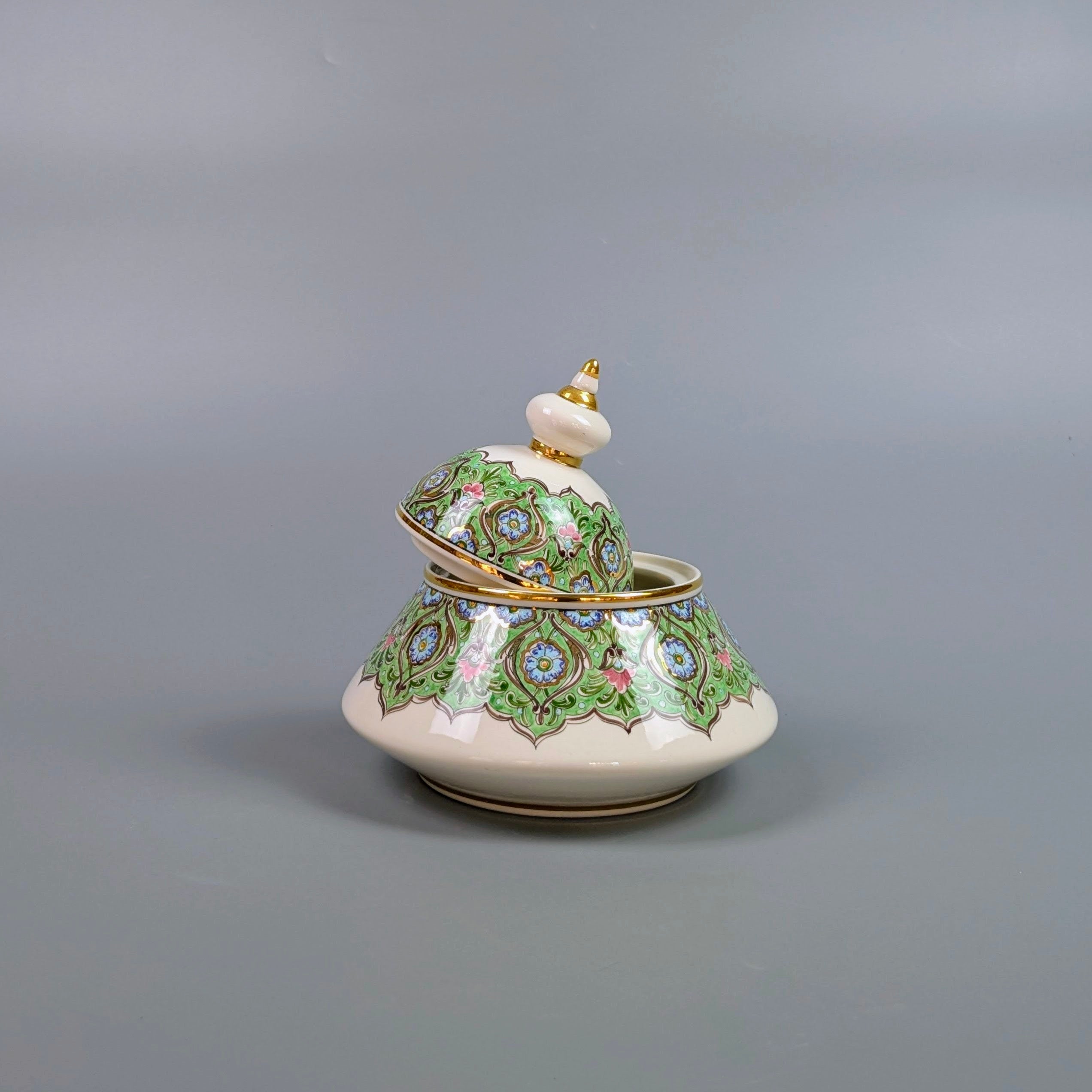 Decorative ceramic container with green floral patterns on a gray background