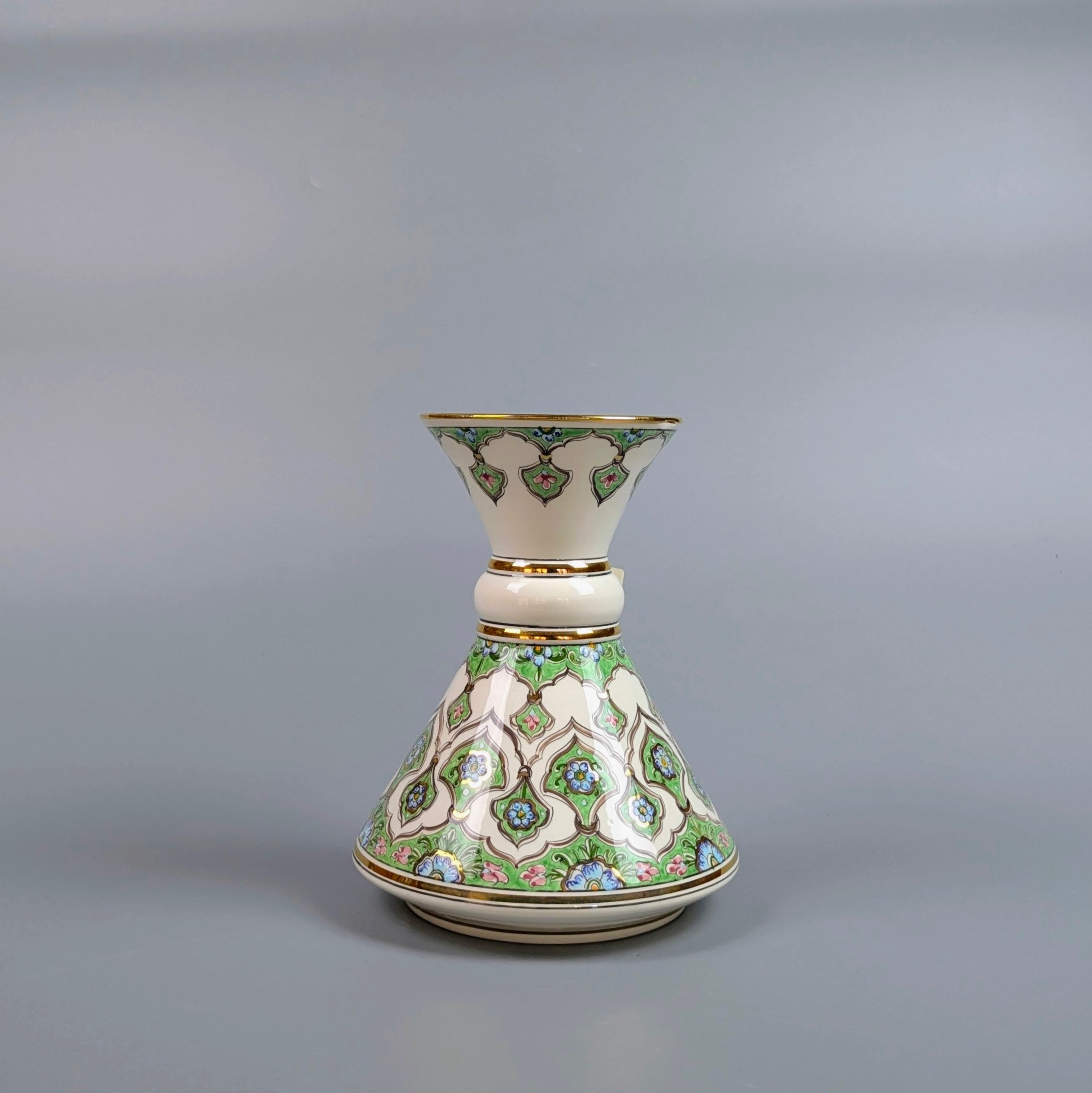 Decorative ceramic vase with intricate green and gold patterns on a gray background