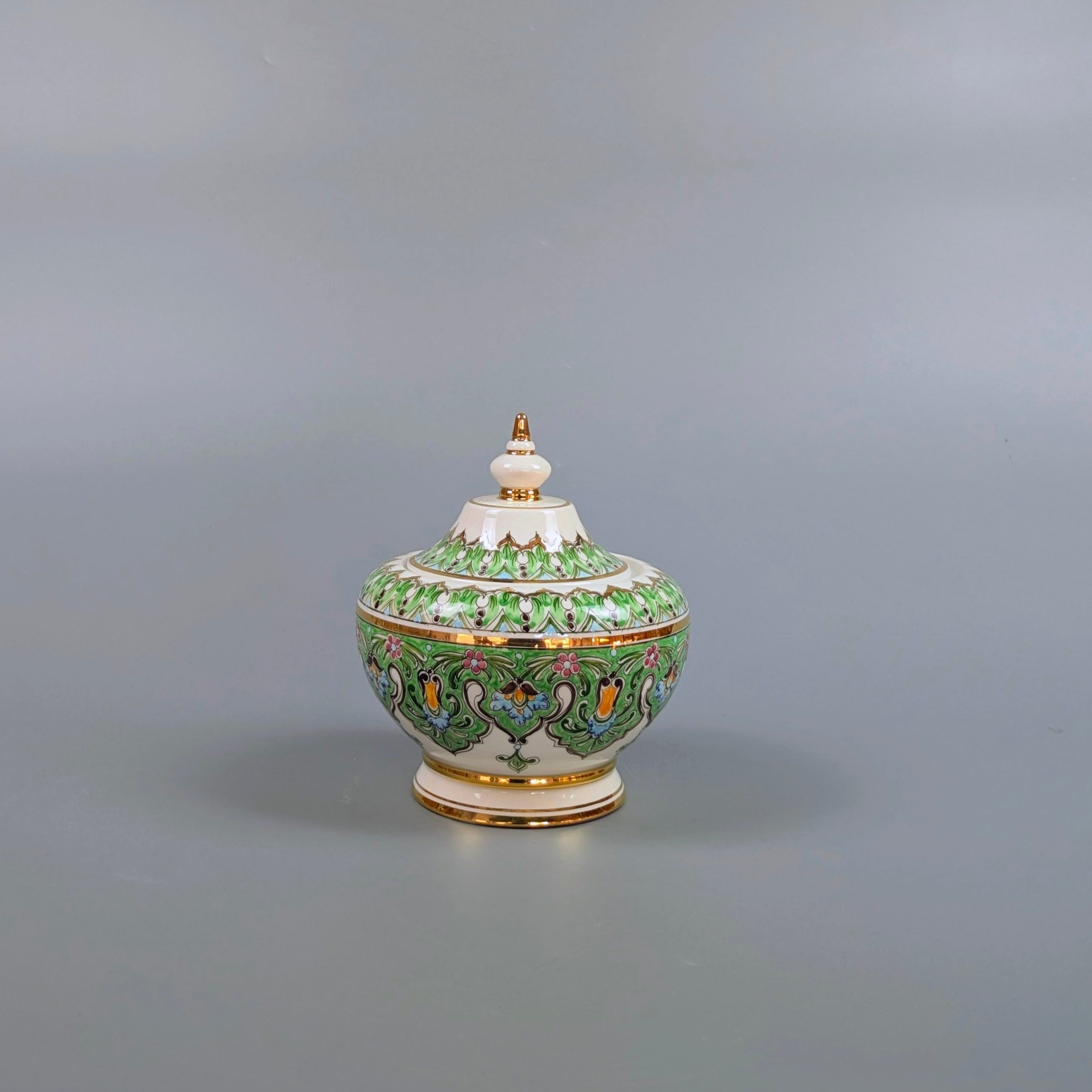Decorative ceramic jar with green and gold patterns on a gray background